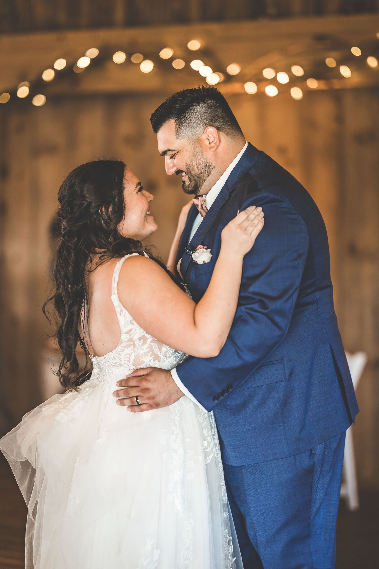 Wedding couple embracing during their first dance in a rustic barn with twinkle lights.