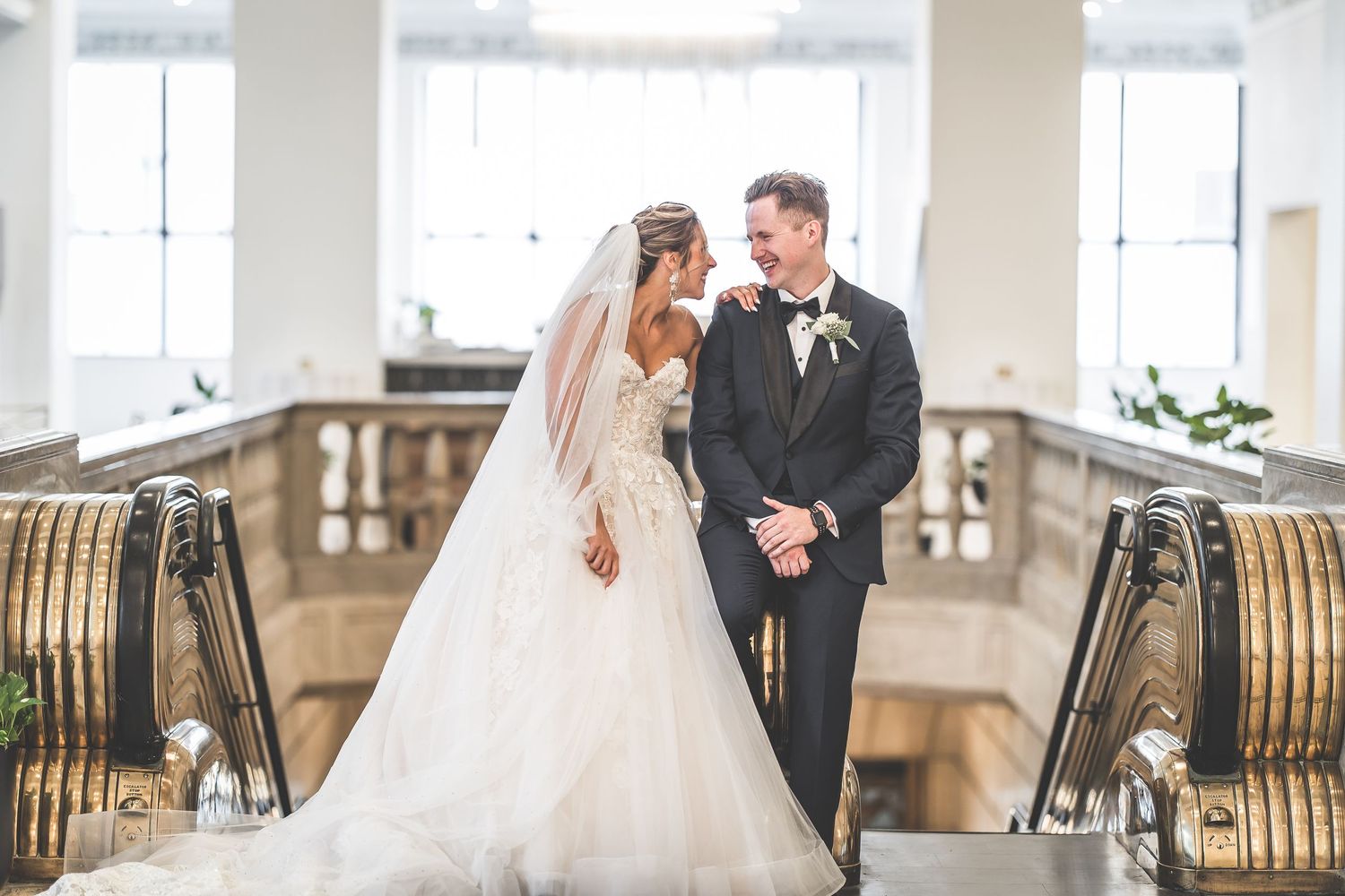 Couple in wedding attire posing in an elegant white ballroom with ornate details.