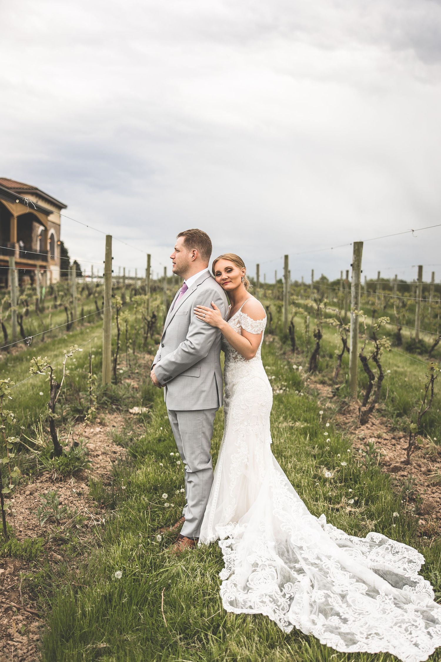 Romantic portrait of newlyweds in vineyard with flowing wedding dress and gray suit.