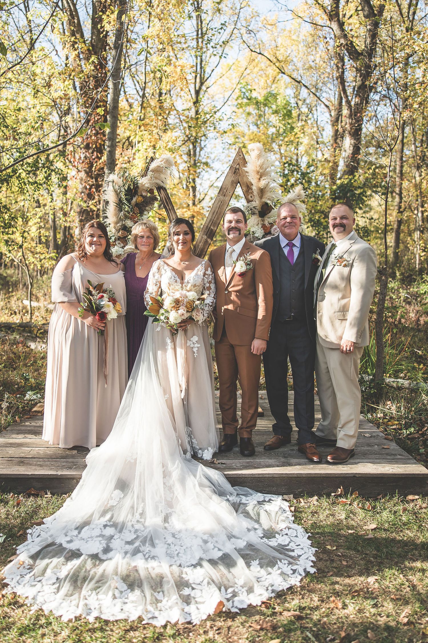 Wedding party poses outdoors in autumn with bridesmaids in neutral dresses and groomsmen in brown suits.