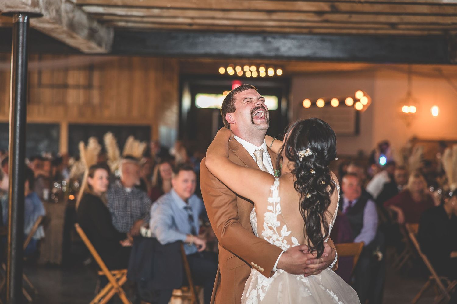 A rustic barn wedding venue with exposed beams and warm lighting during a reception dance.