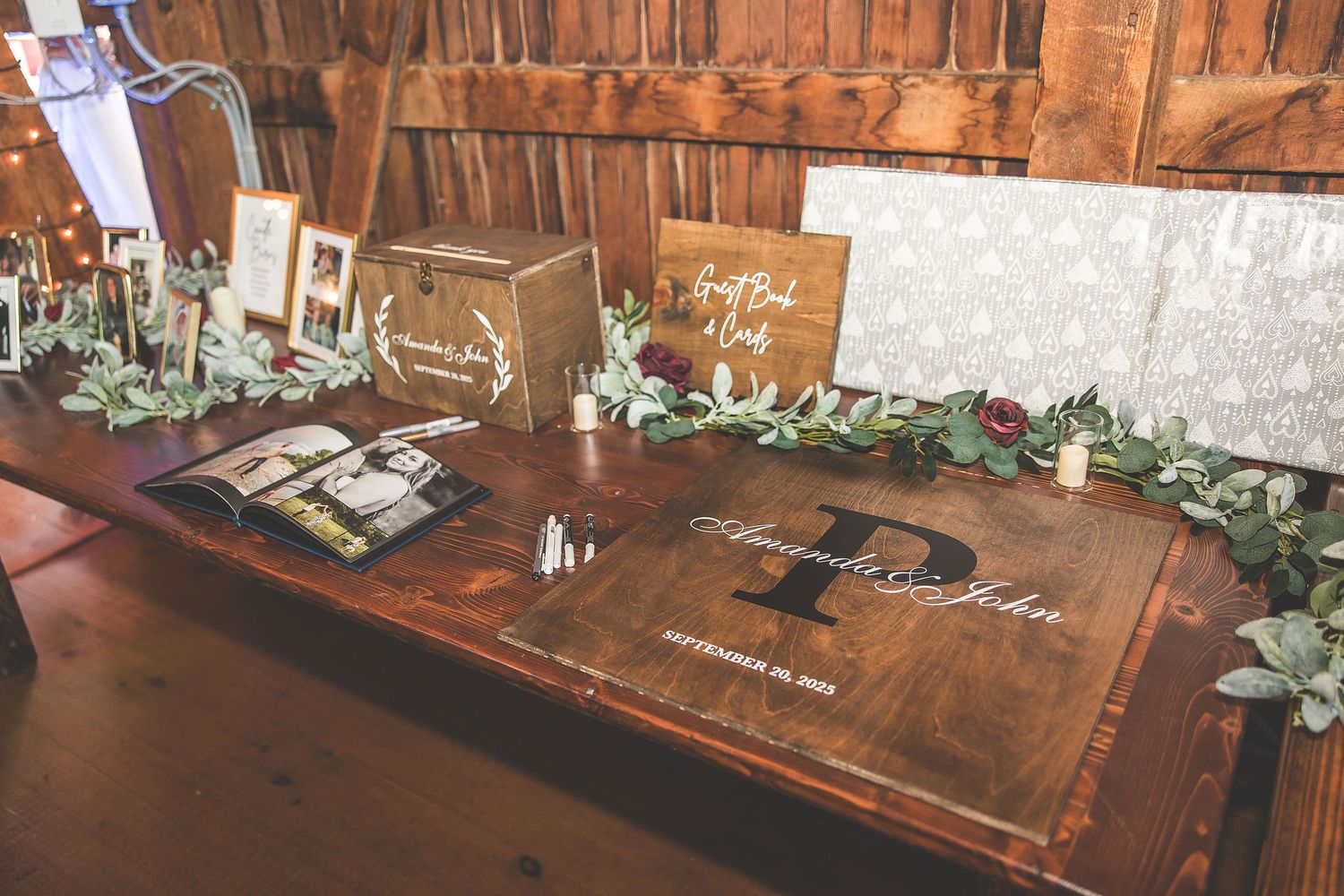 Wooden tables decorated with greenery and white linens in a rustic barn reception venue.