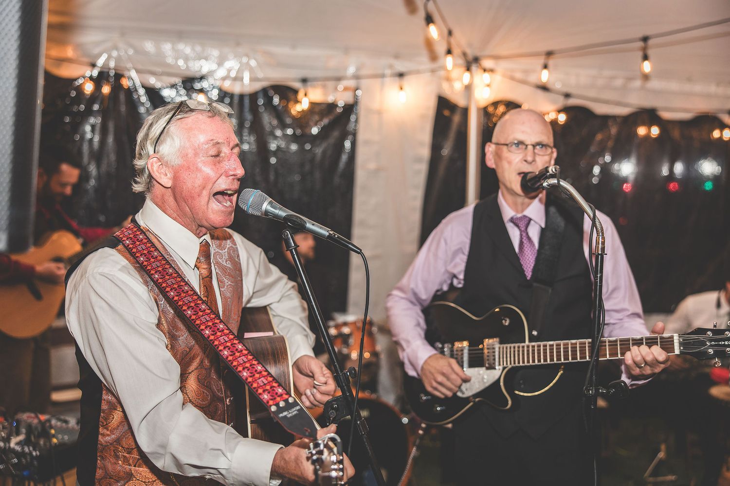 Live band performs with guitars and instruments at a wedding reception under string lights.