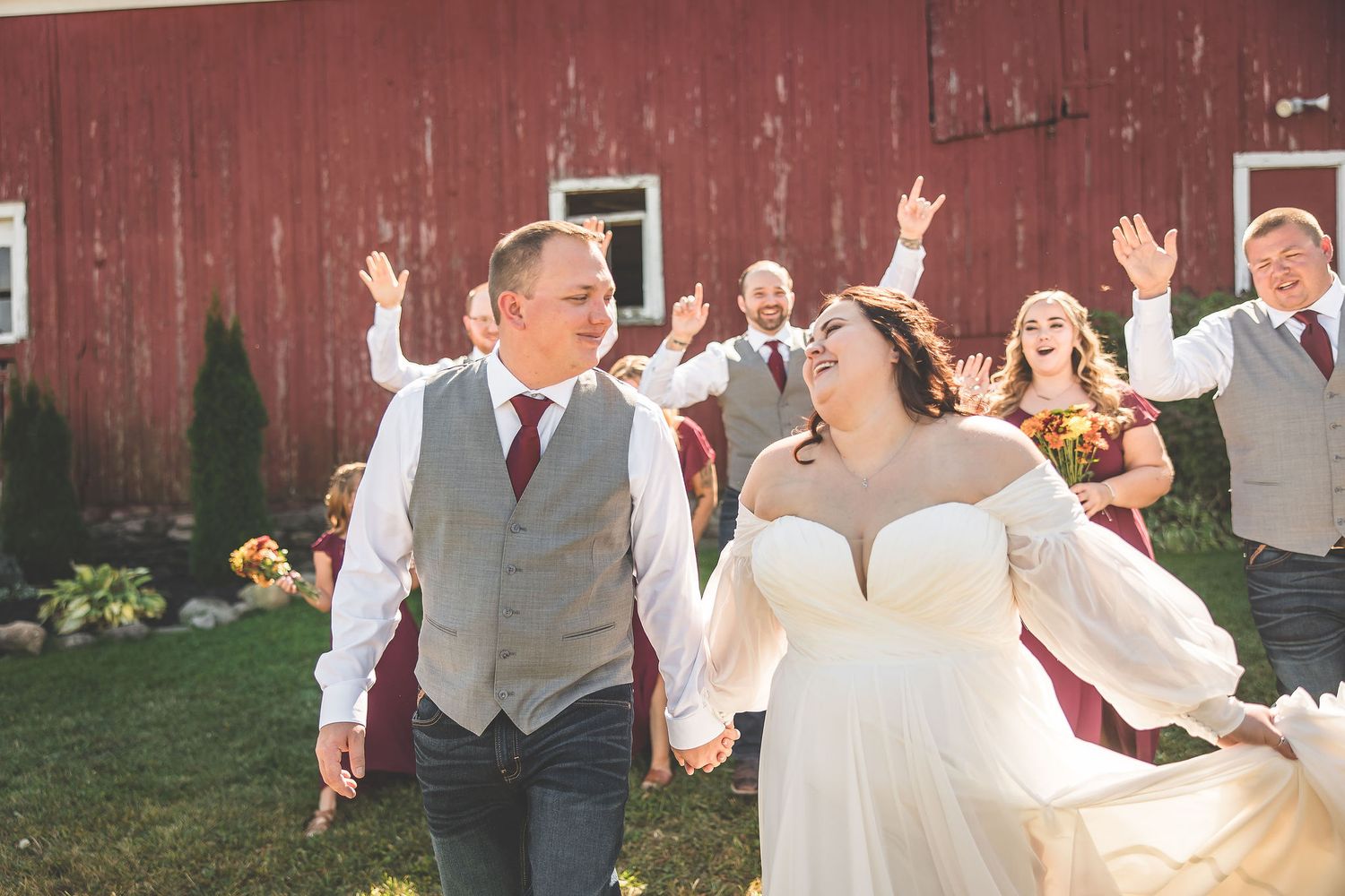 Wedding party having fun with playful poses against rustic barn setting.