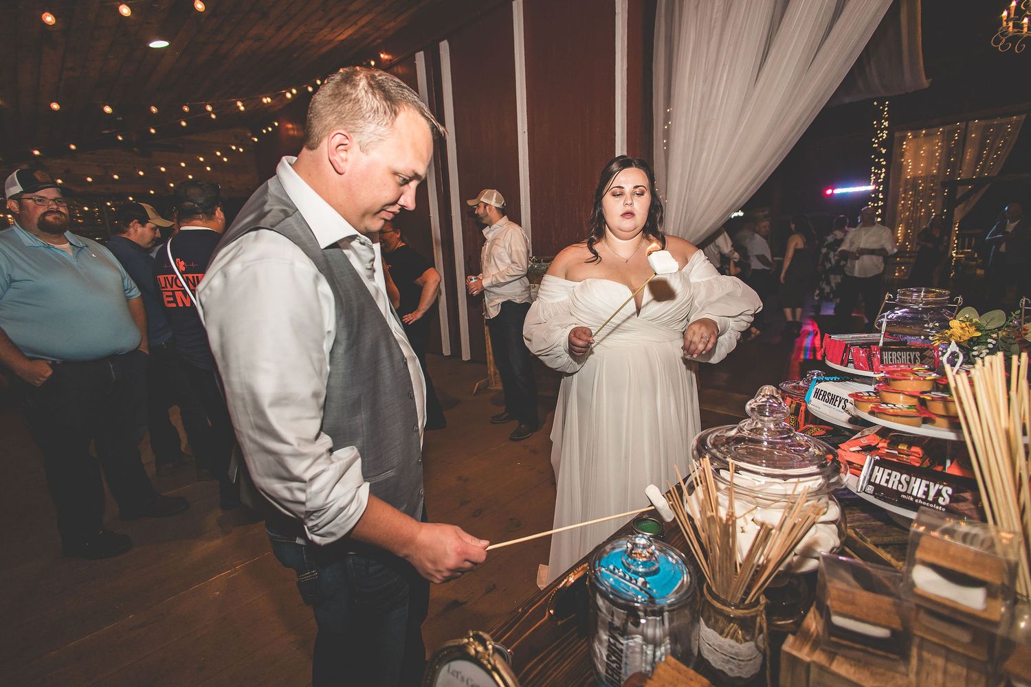 Guests browse a dessert and refreshment table at an elegant barn reception.