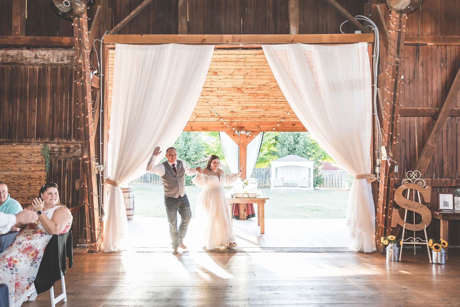 Couples dance together in a rustic barn venue decorated with elegant white drapes and chandeliers.