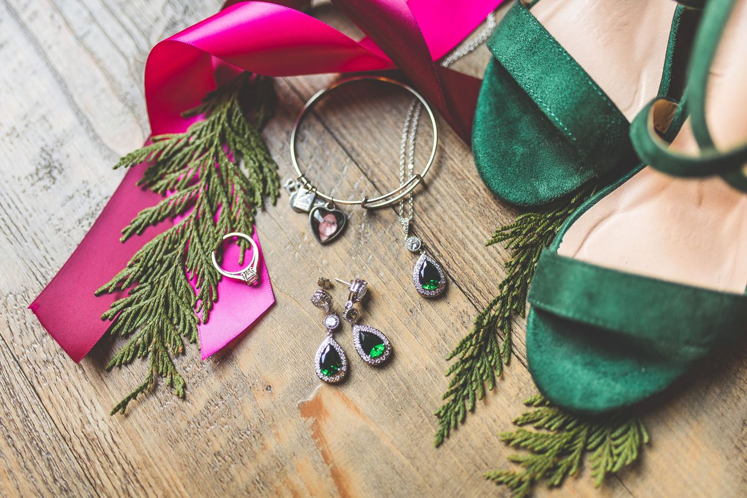 Pink and green wedding accessories arranged on rustic wooden surface.