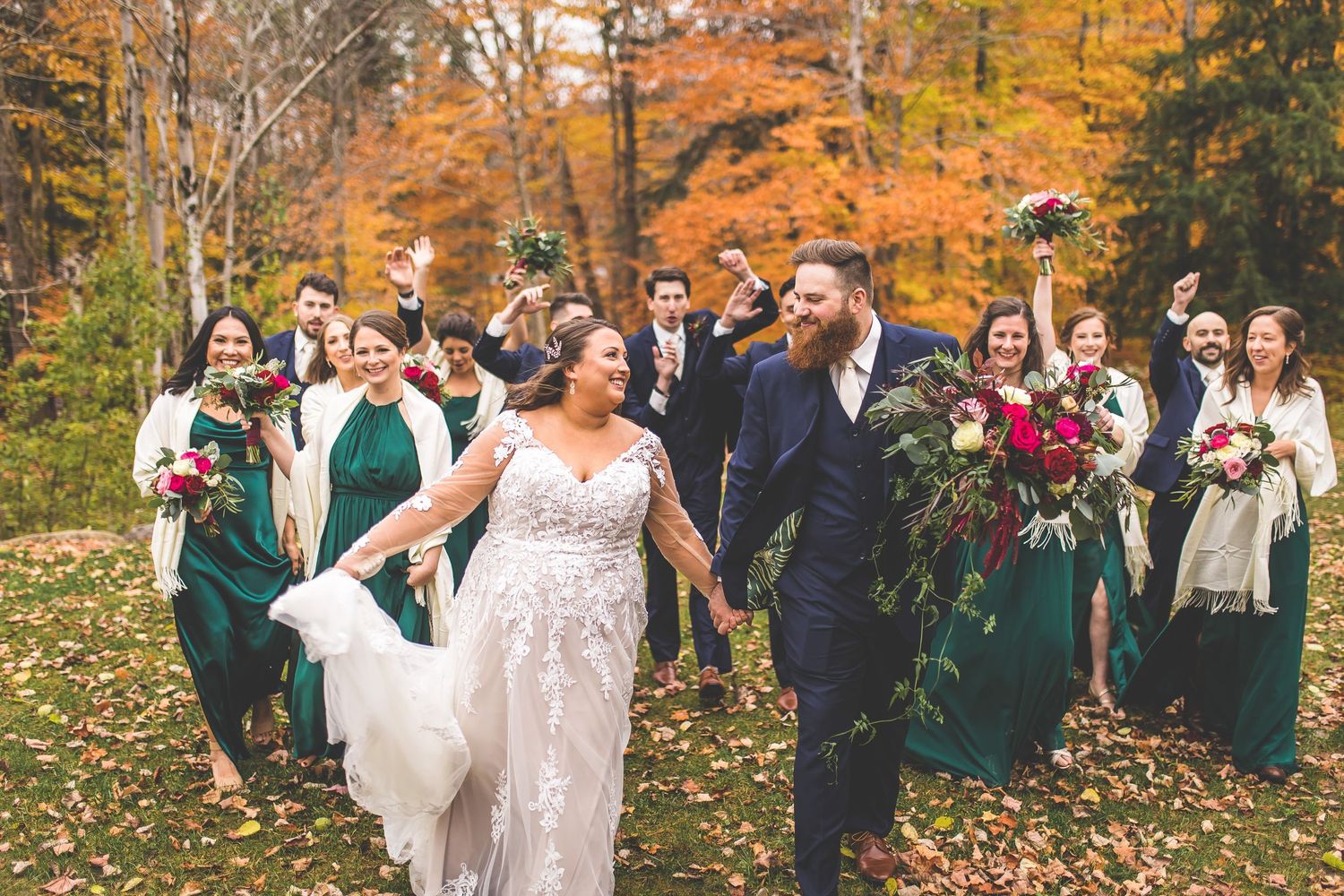 Wedding party stands together in a beautiful autumn forest setting with vibrant orange foliage.