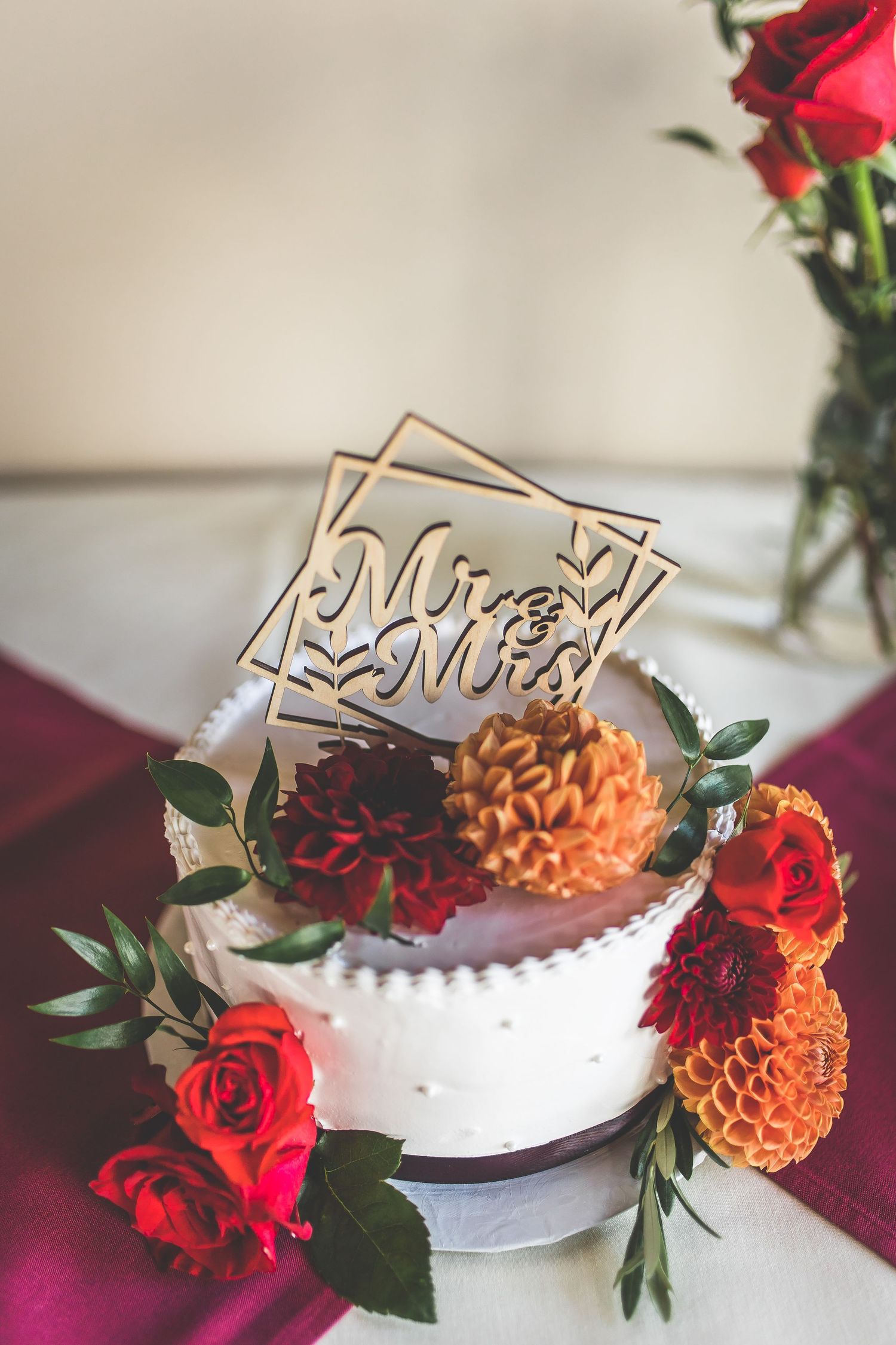 Wedding cake decorated with red roses and orange dahlias with wooden cake topper.
