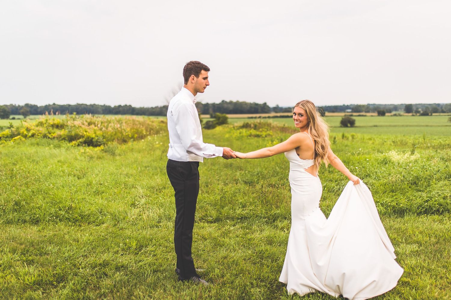 Wedding couple poses in a scenic field with natural landscape backdrop.