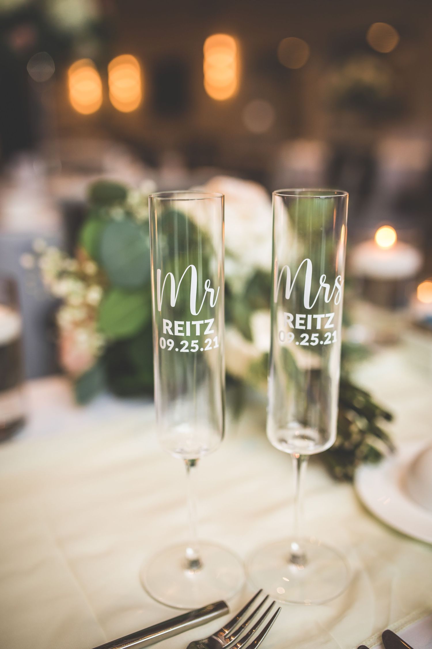 Personalized wedding champagne glasses with custom date engraving on white tablecloth.