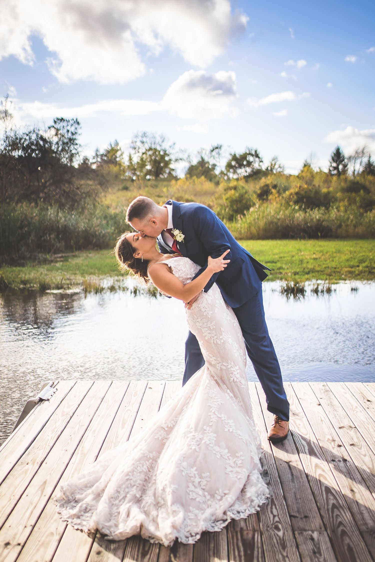Newlyweds dance and embrace on a lakeside dock during their wedding photoshoot.