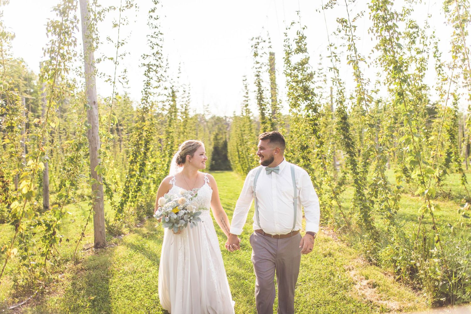 Couple walking through sunny hop fields during outdoor wedding photo session.