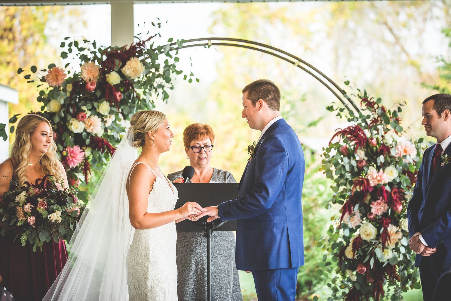 Wedding ceremony under a floral arch with burgundy and peach blooms during an intimate outdoor celebration.