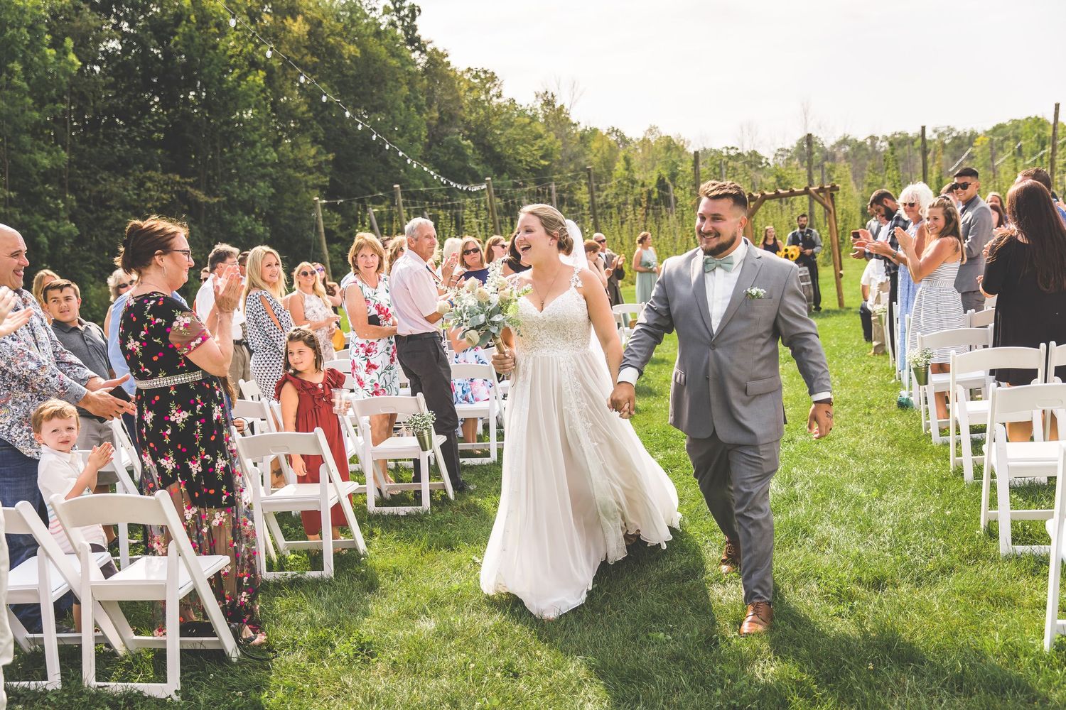 Outdoor wedding ceremony setup with white chairs on grass surrounded by natural landscape.