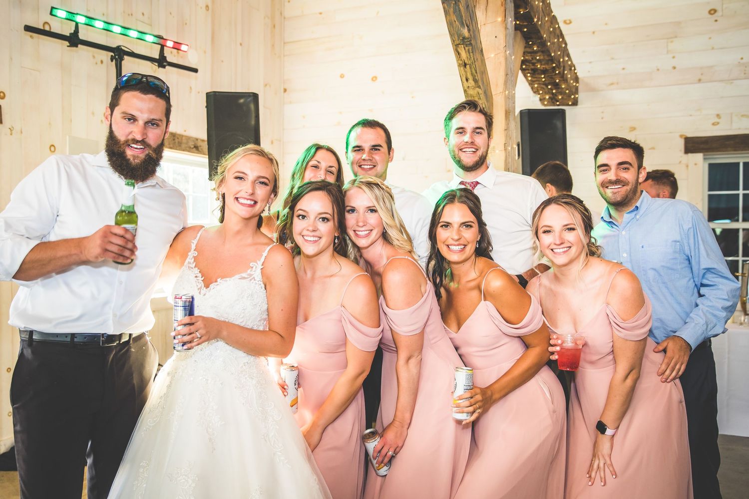 Wedding party poses together in pink bridesmaid dresses at a rustic venue.