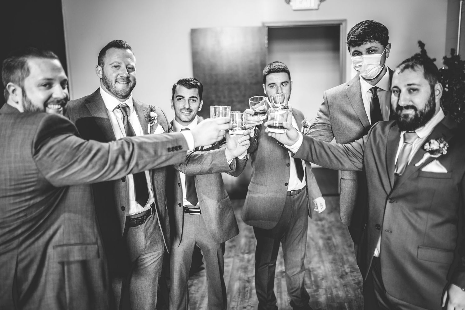 Wedding party members laugh and joke together during pre-ceremony preparations in a casual indoor setting.