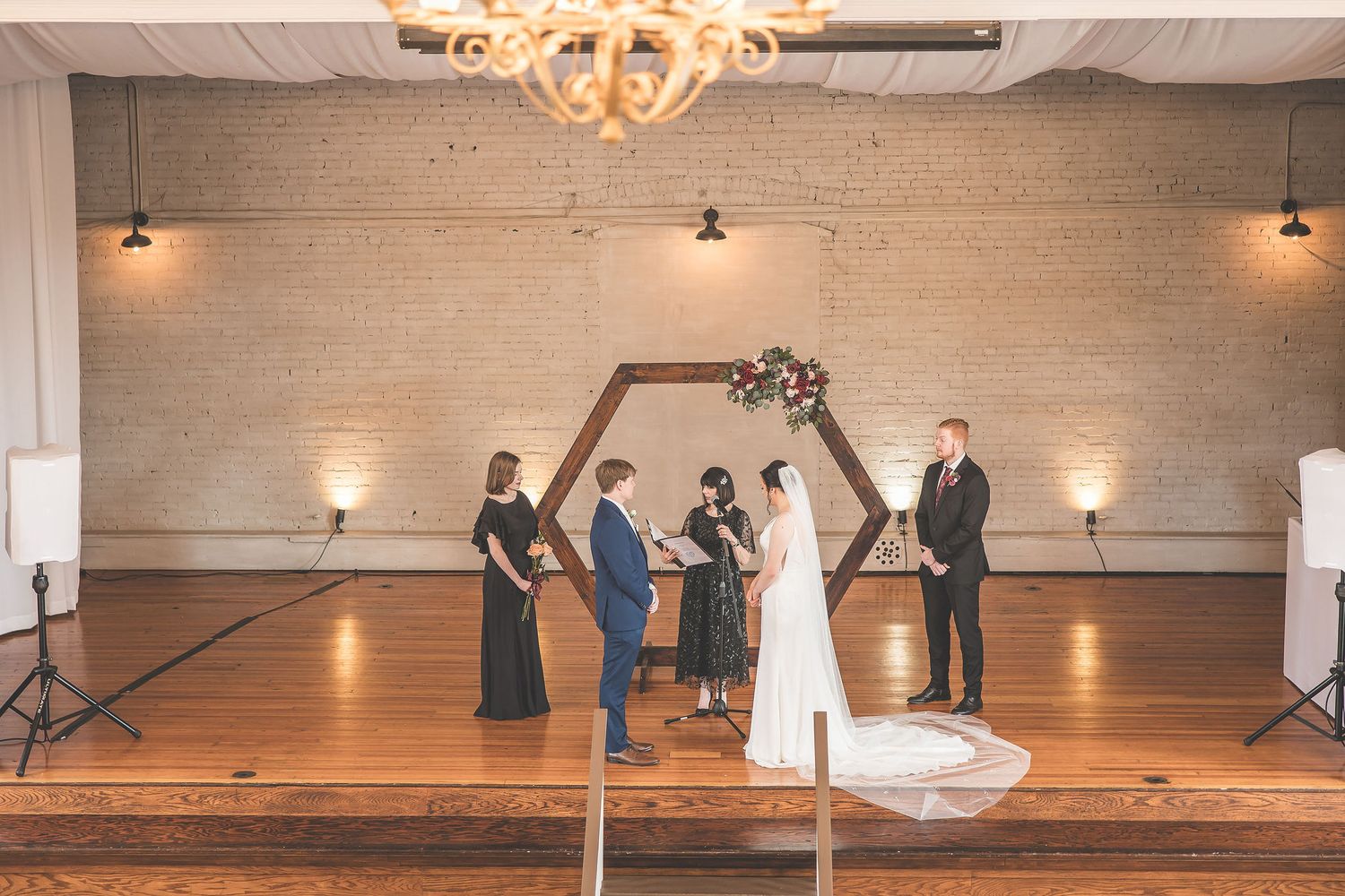 Wedding venue interior showing hardwood floors and exposed brick walls with decorative lighting.