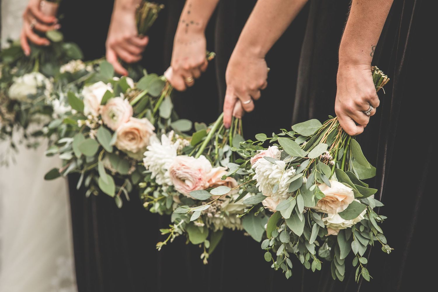 Close-up of elegant wedding bouquets with white roses and greenery held by bridal party.