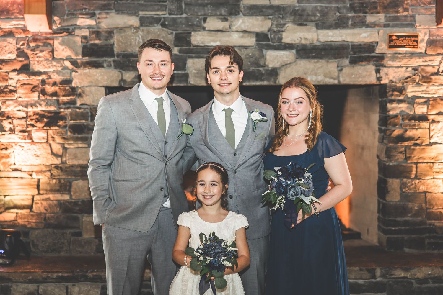 Small wedding group poses together in front of stone fireplace.