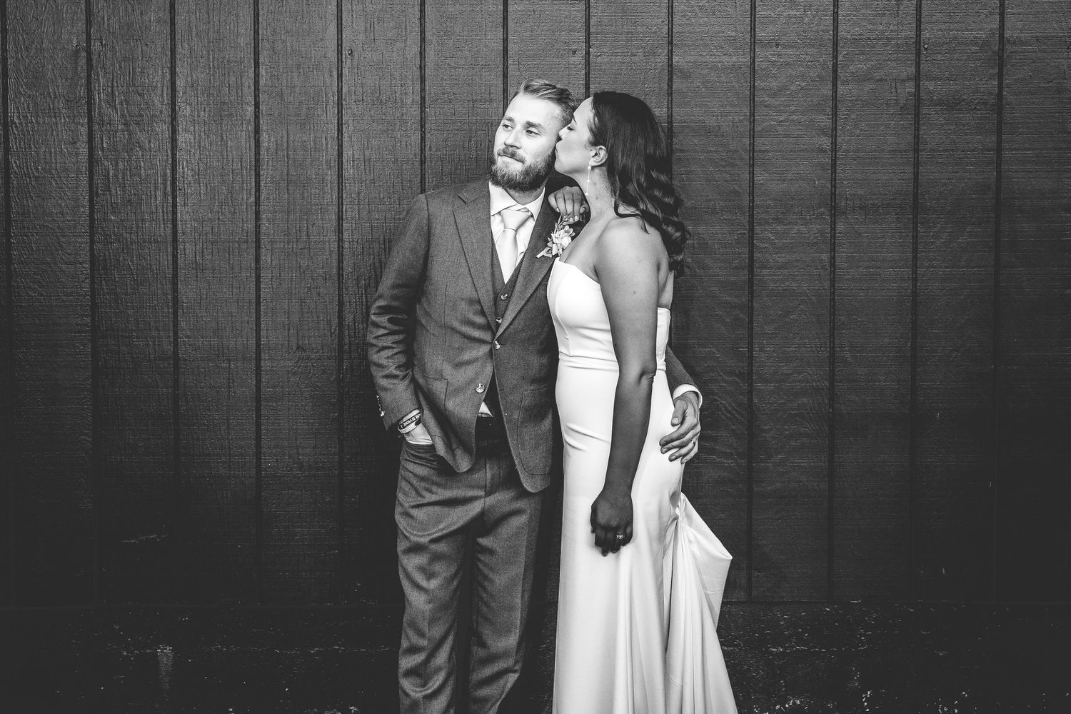 A black and white portrait of a couple posing against a dark wooden wall.