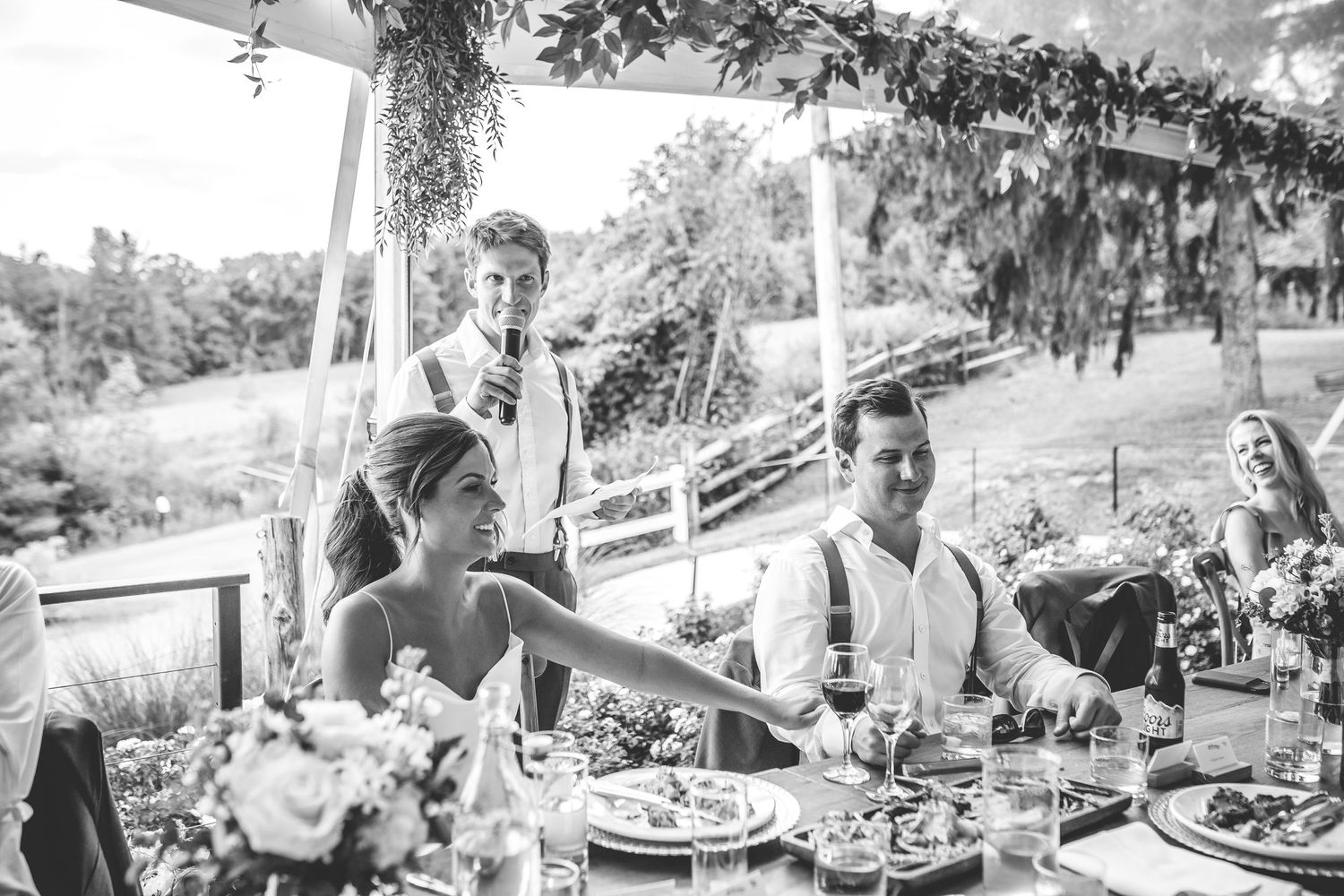 Wedding reception dinner party with guests seated at long tables under a covered outdoor venue.