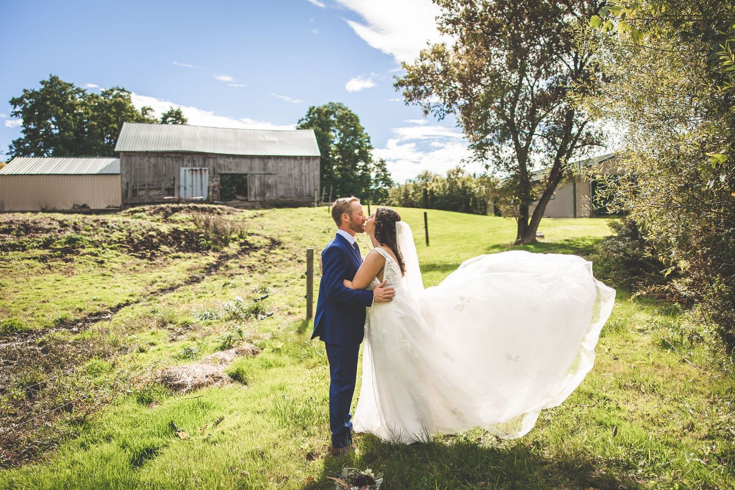 Wedding couple posing in a scenic countryside setting with rolling hills and blue skies.