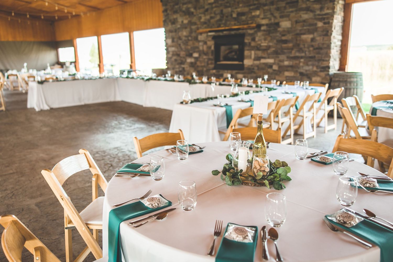 Wedding reception venue with white linens and teal accents set up in a rustic stone room.