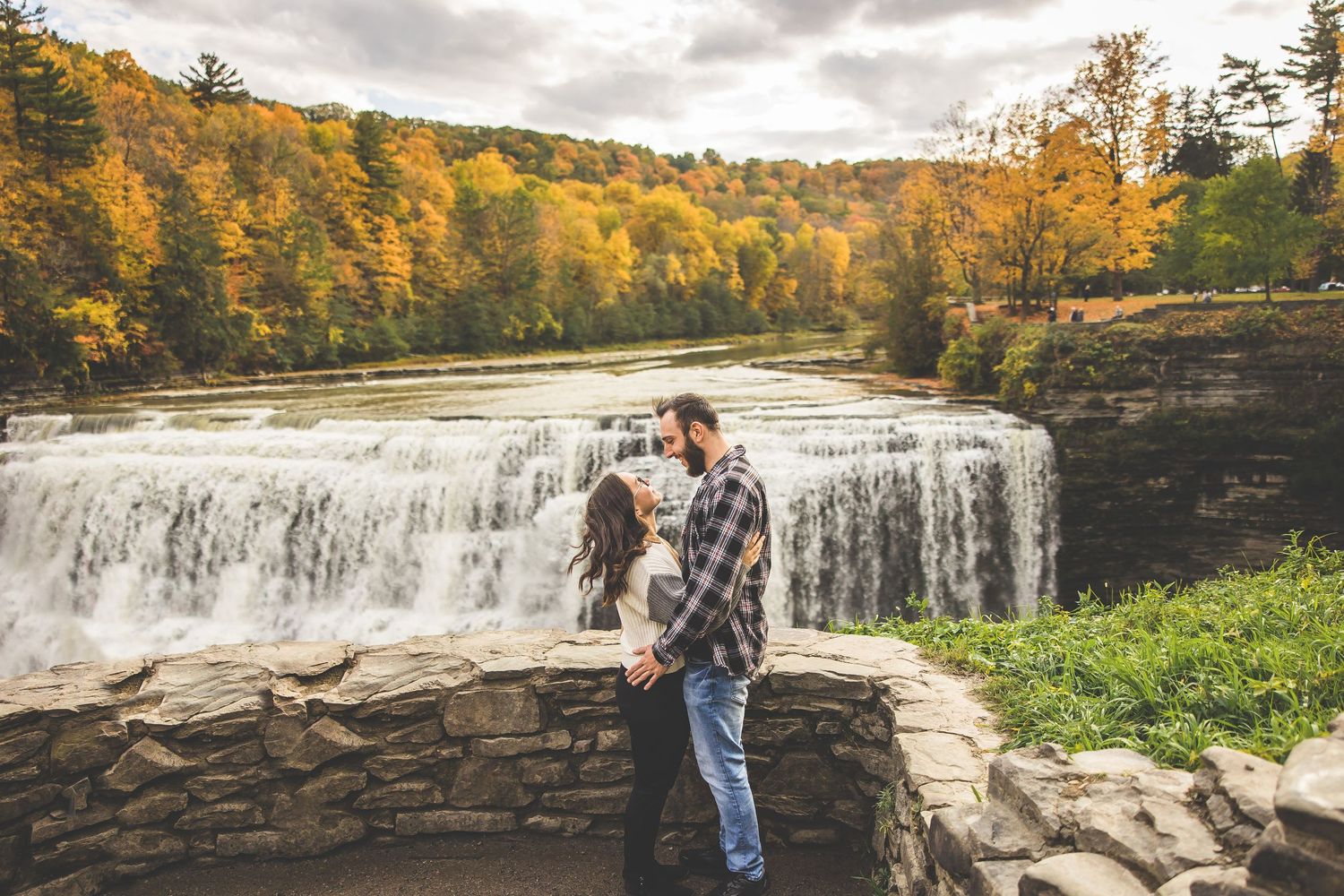 Dramatic waterfall creates stunning backdrop for romantic autumn engagement photos.