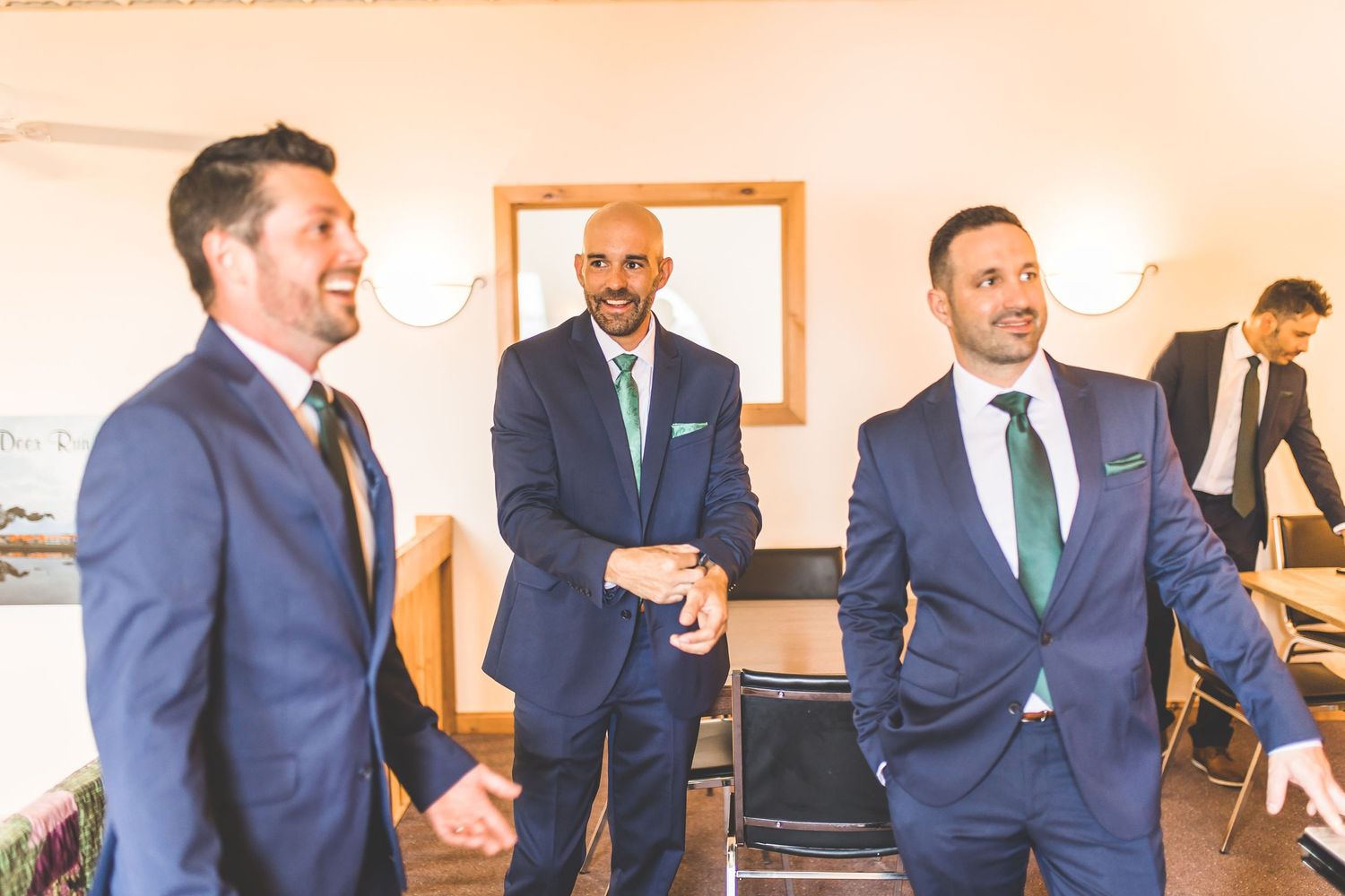 Groomsmen in navy suits with green ties pose together at rustic venue.