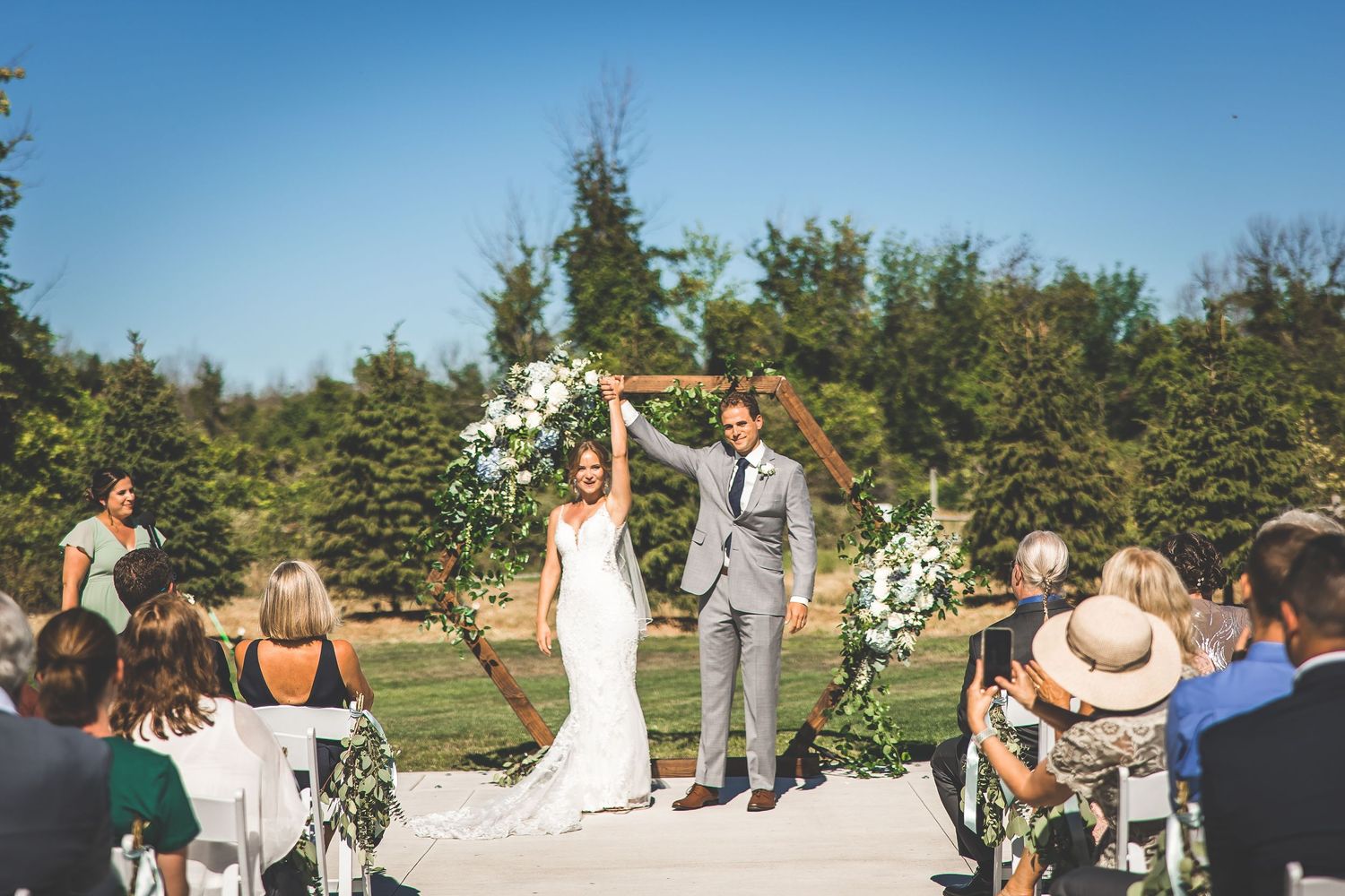 Wedding guests seated in white chairs during an outdoor ceremony with natural landscape backdrop.
