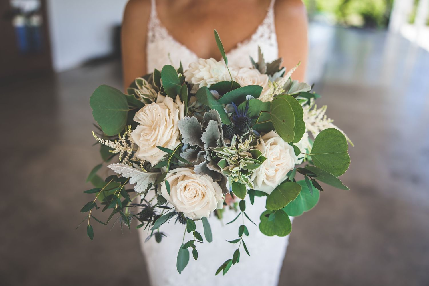 Close-up of white rose and eucalyptus wedding bouquet against lace dress.