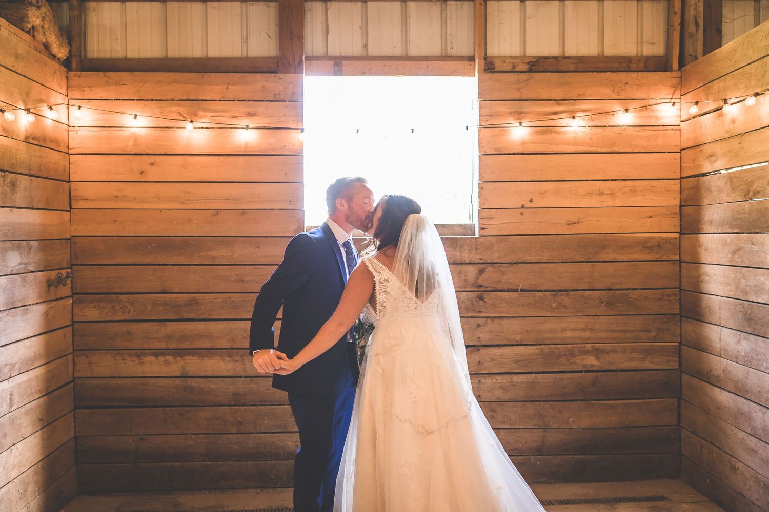 String lights illuminate a rustic wooden barn interior creating a romantic wedding atmosphere.
