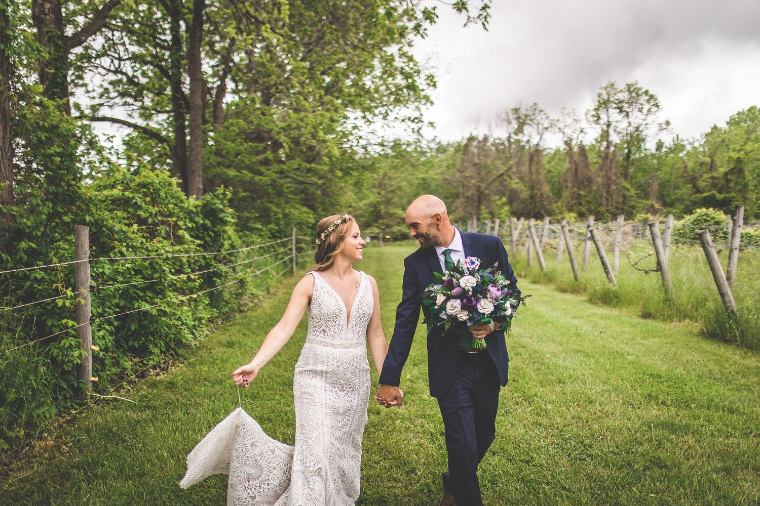 A candid wedding photo of a couple walking through a green garden path.