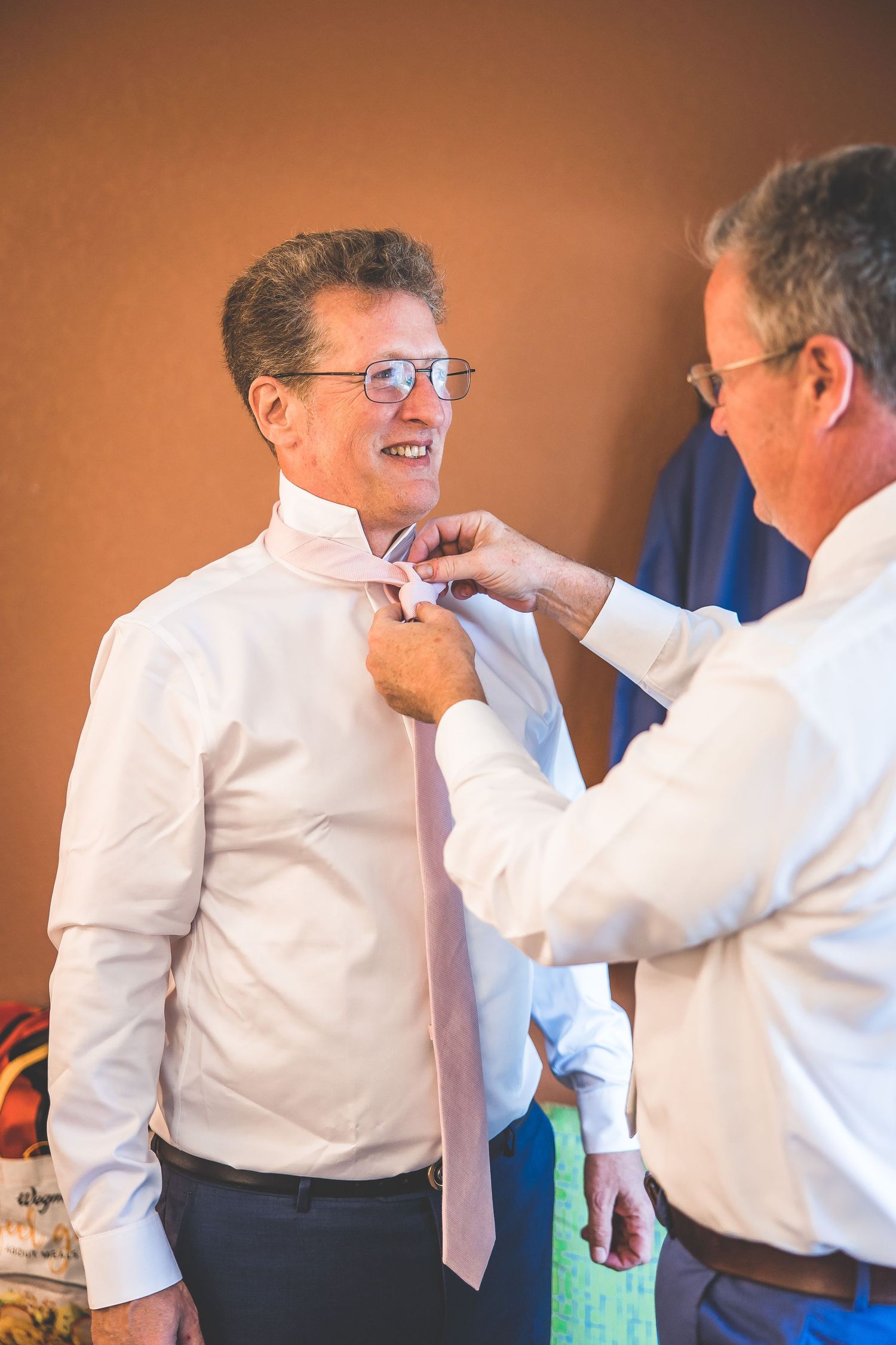 A man helps adjust another man's tie before a formal event.