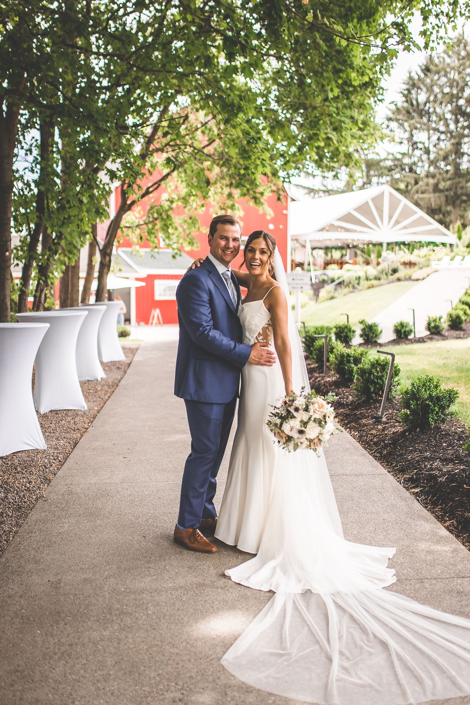 Wedding couple poses together on a garden path with a red barn in the background.