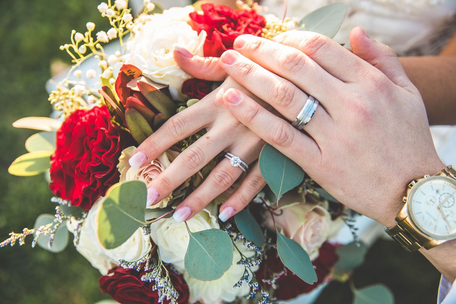 Close-up of hands showing wedding rings with red and white floral bouquet details.