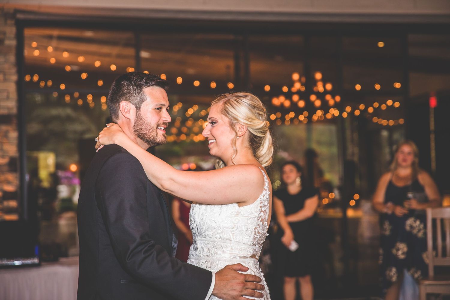 Couple sharing their first dance in a rustic venue with string lights overhead.