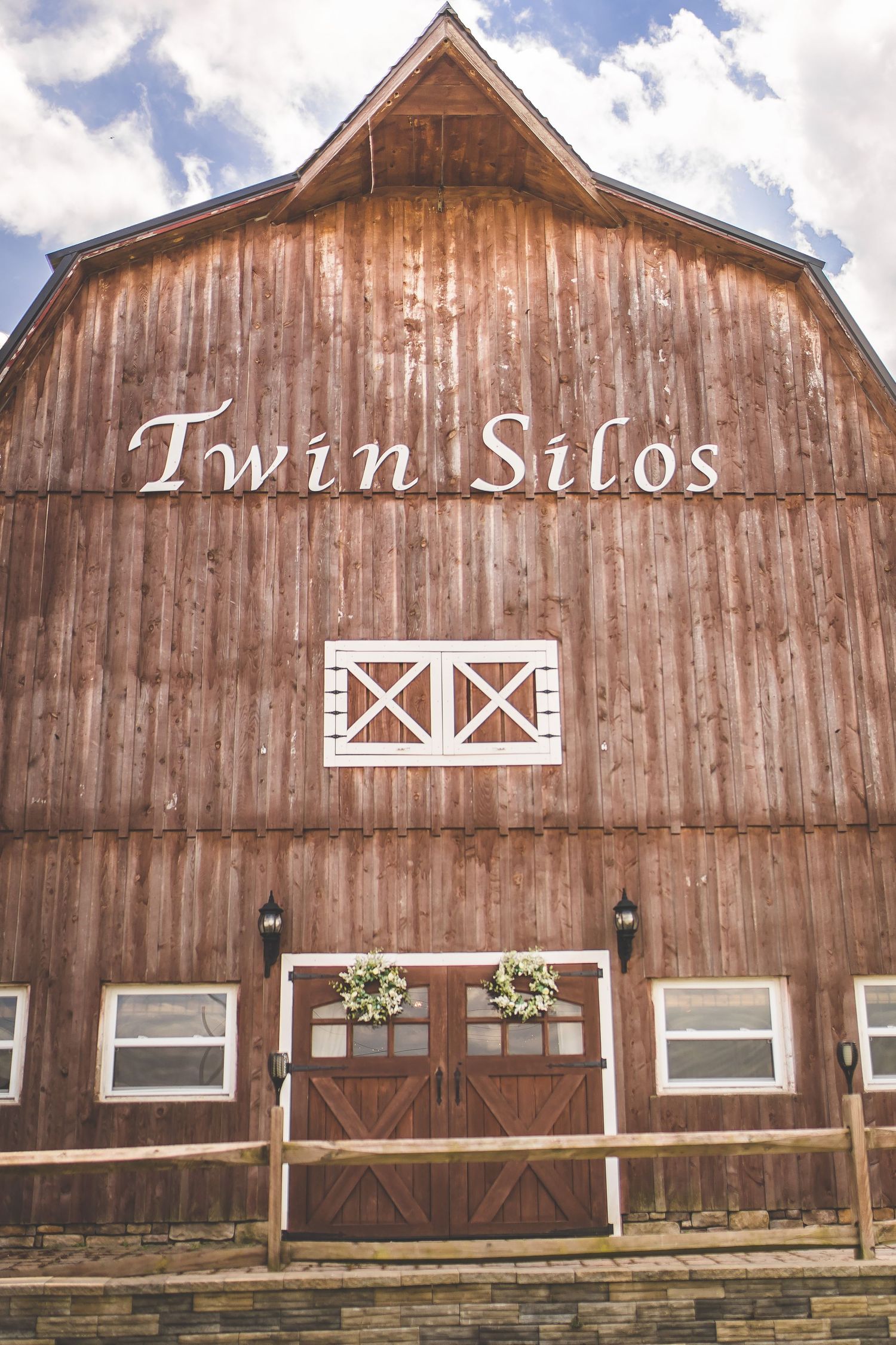 Rustic wooden barn venue with 'Twin Silos' signage against blue sky.