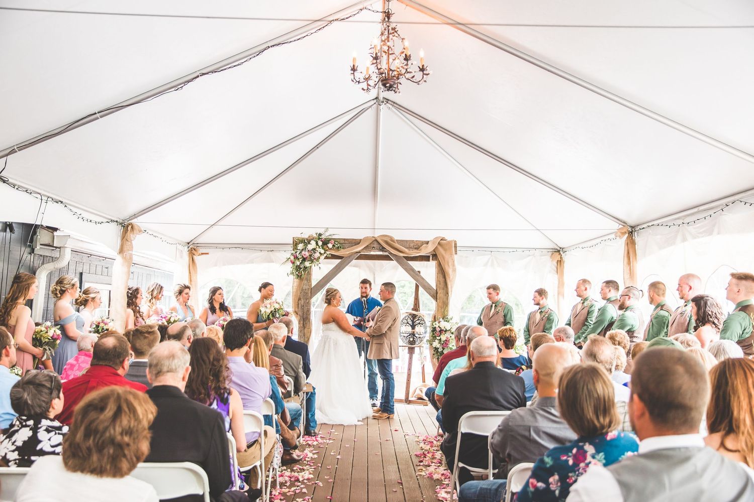 Wide view of wedding ceremony under white tent with rows of guest seating.