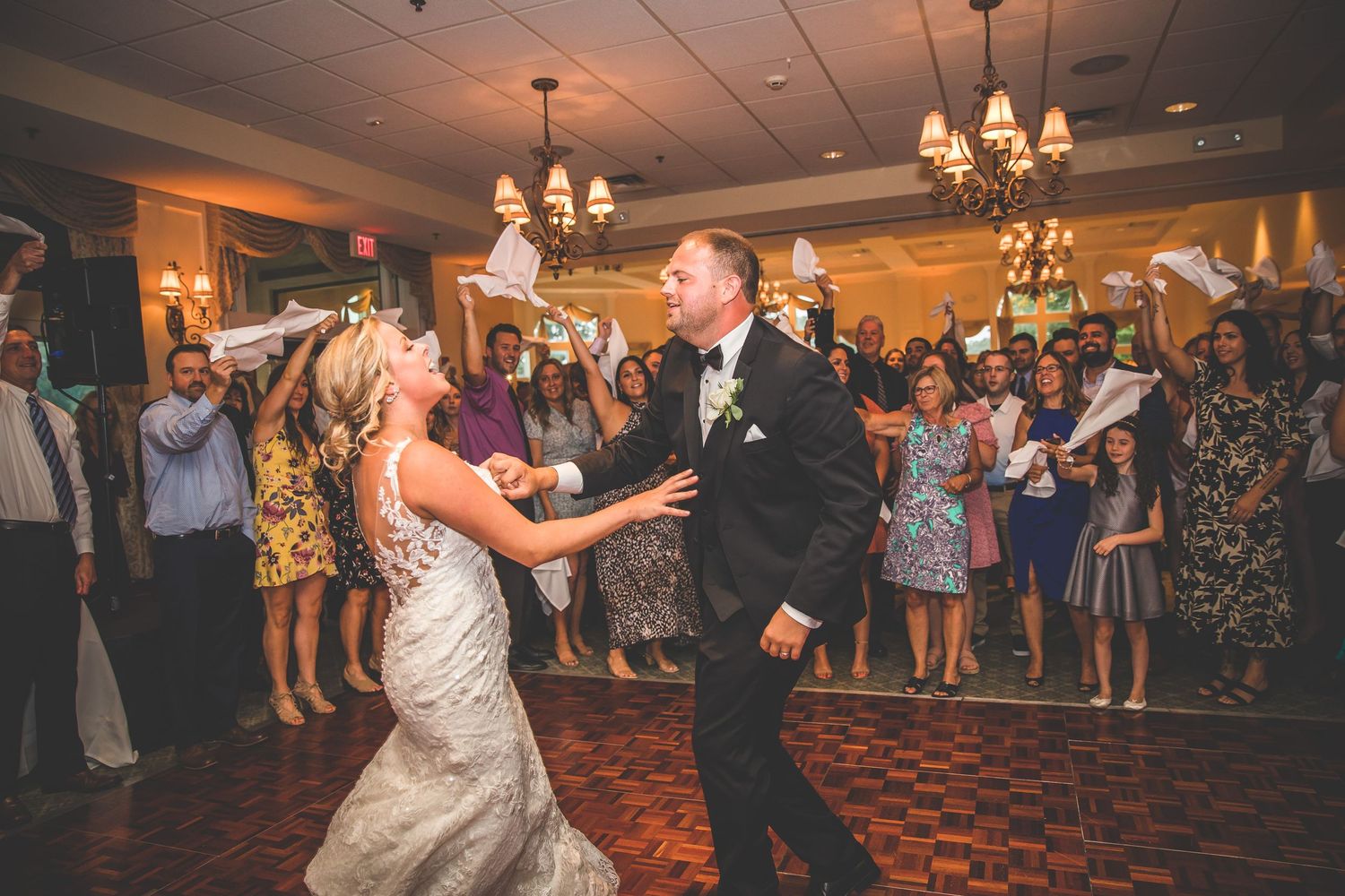 A couple performs their first dance surrounded by guests on a patterned ballroom floor.
