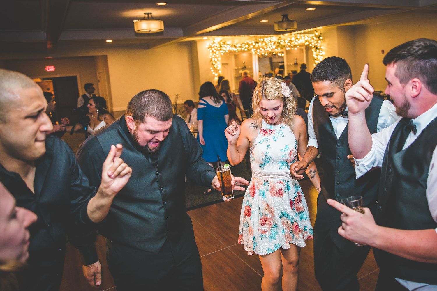 Wedding guests dancing and celebrating at an indoor reception with string lights.