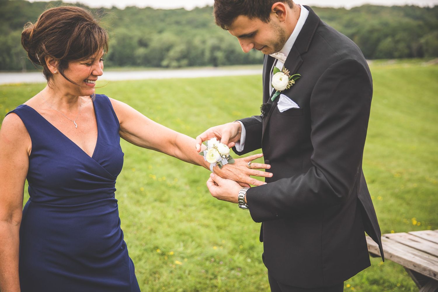 Wedding party members pin boutonnieres on formal attire outdoors.