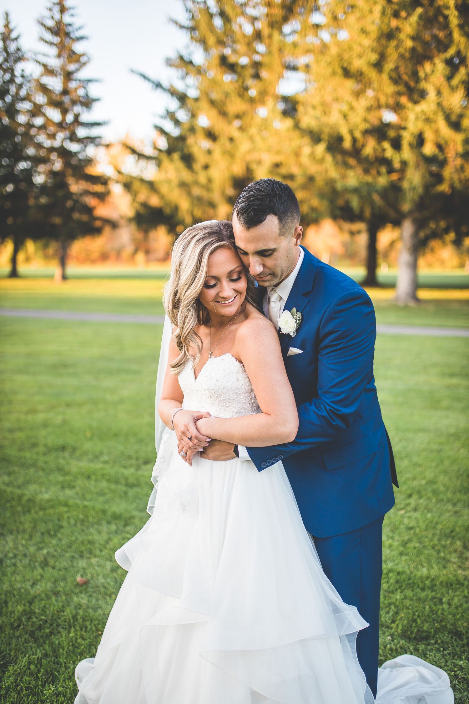 Romantic couple embracing in formal attire on manicured lawn during golden hour.