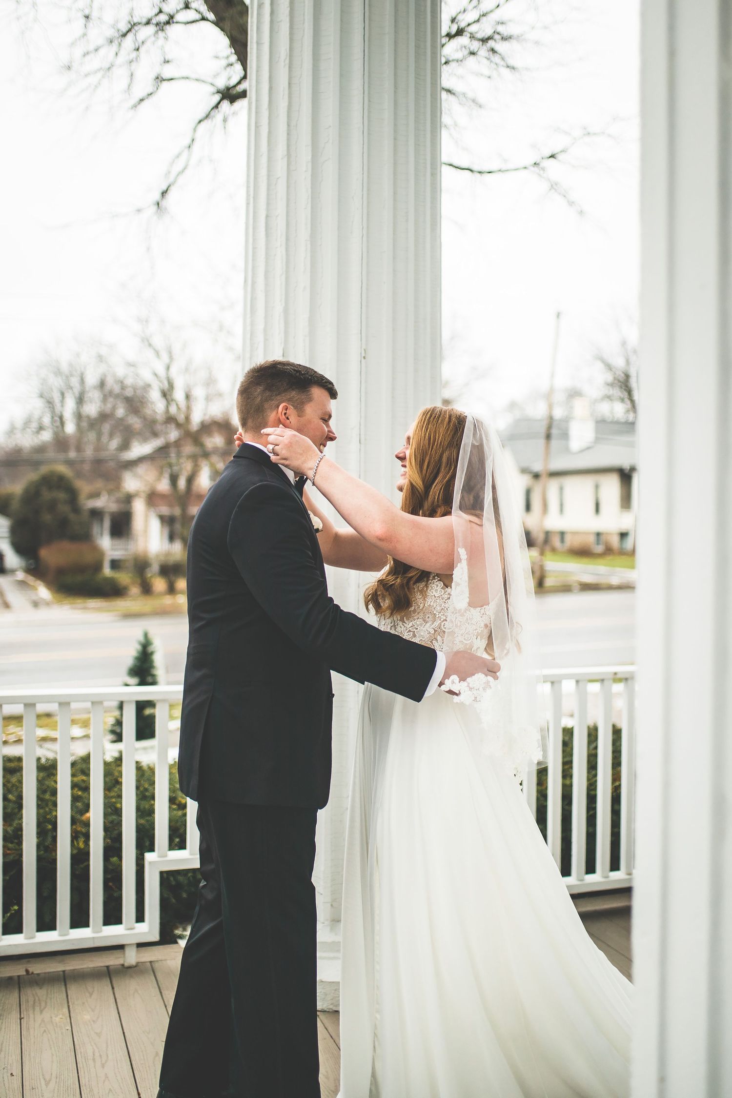 A couple sharing their first look moment between white columns on a porch.