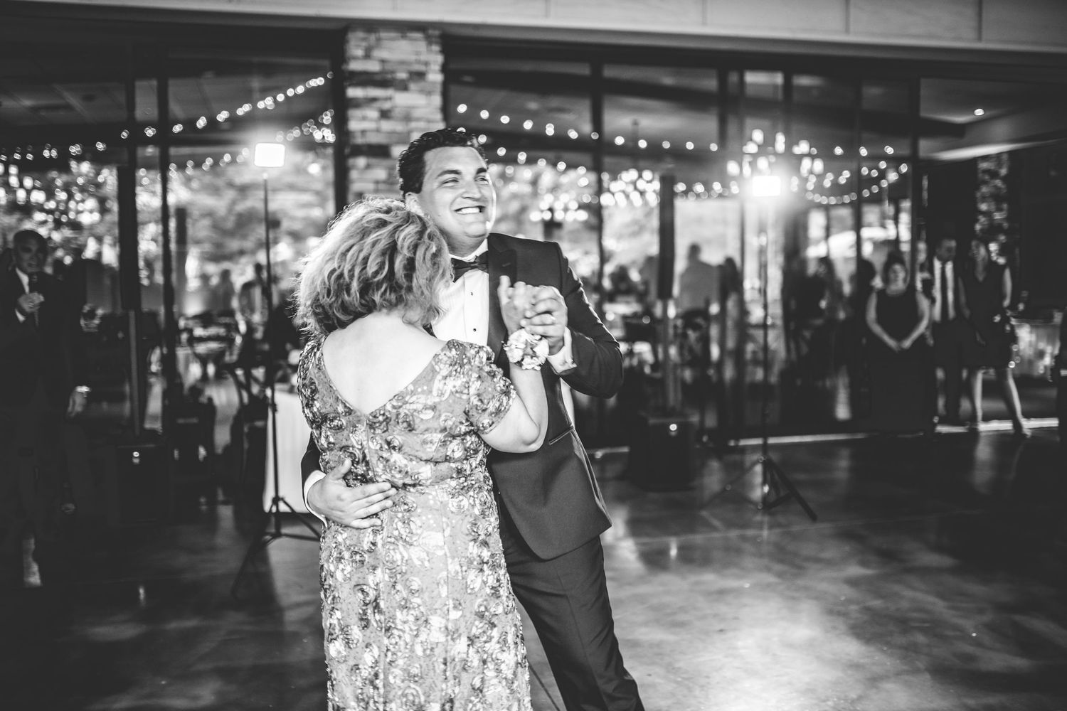 Black and white photo of dancing at wedding reception with decorative lights and stone columns.