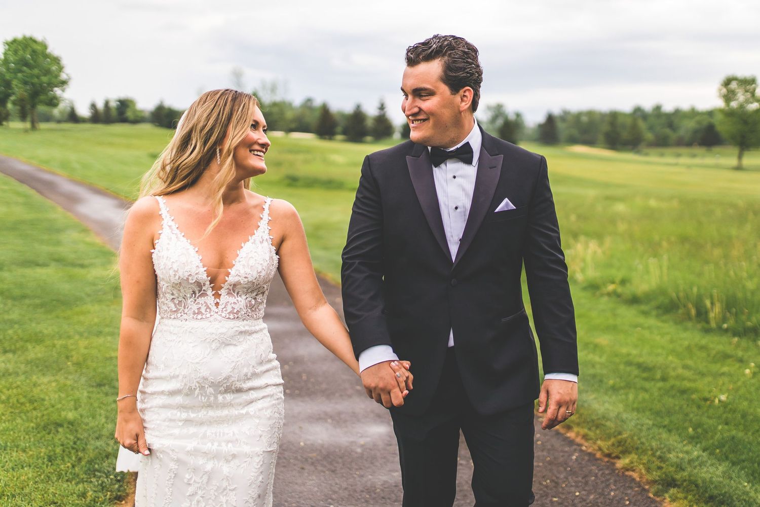 Bride and groom walk hand in hand across scenic golf course during wedding photos.