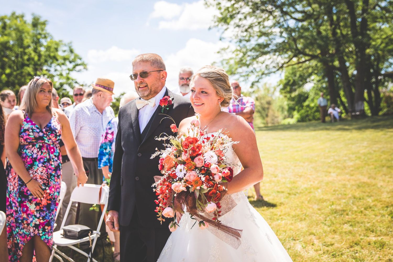Wedding ceremony guests gather on a sunny hillside for an outdoor celebration.