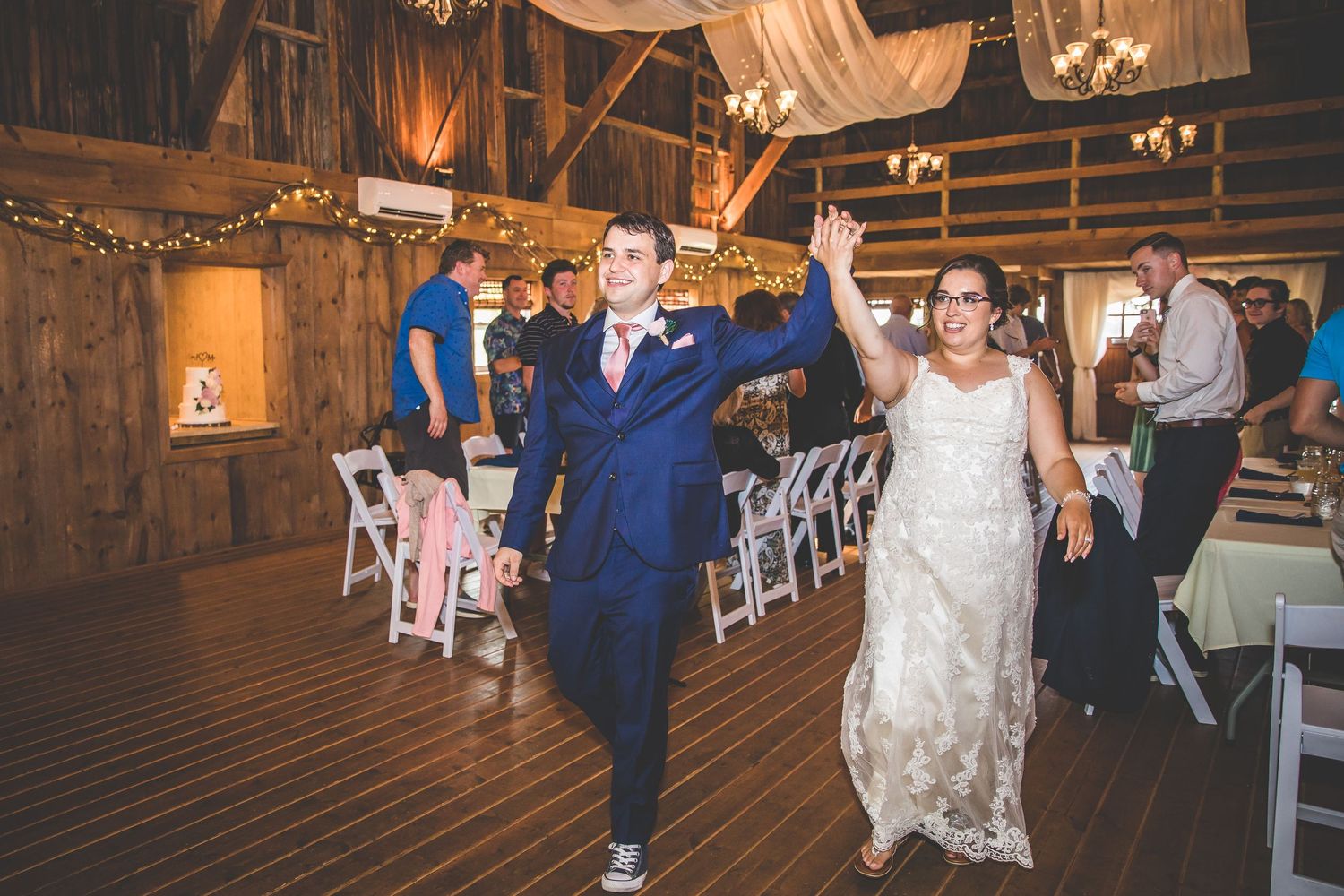Wedding celebration with dancing guests inside a barn decorated with white drapery.