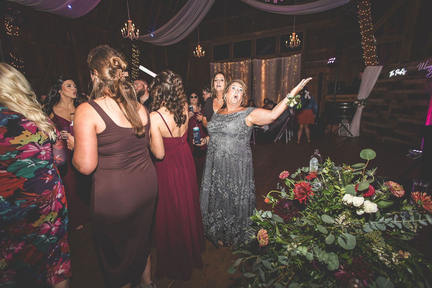 Wedding party dancing and celebrating in a barn venue with decorative lighting and draping.